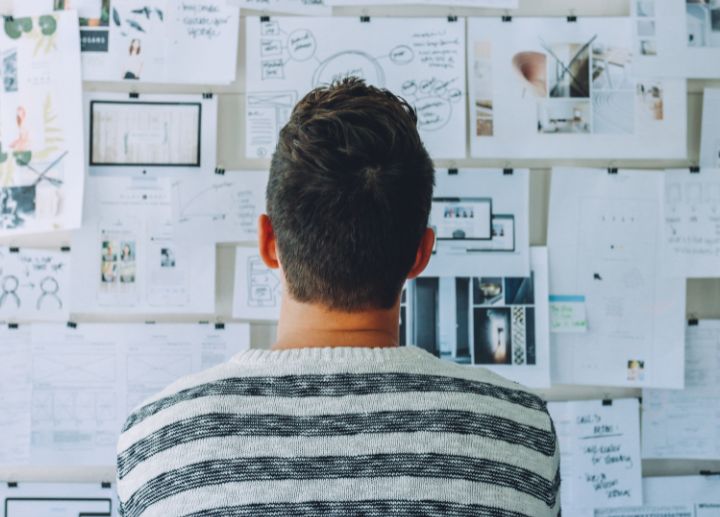 Person looking at a wall covered with papers, diagrams, and notes.